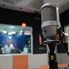 Fotografia mostra um estúdio de rádio, com um microfone em primeiro plano.