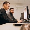 Foto quadrada: dois homens brancos, de cabelos escuros, trabalhando diante computadores