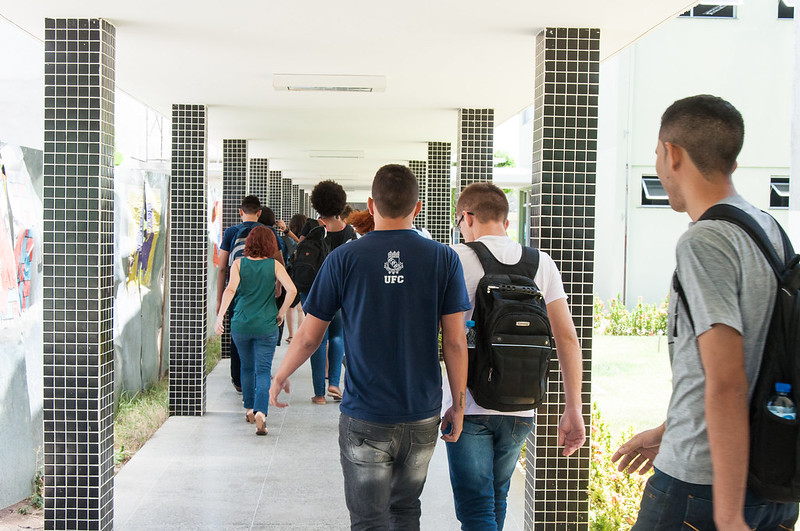 Fotografia horizontal colorida: Grupo de estudantes caminha pelo corredor de um bloco da Universidade.