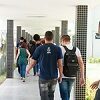 Foto quadrada. Grupo de estudantes caminha no corredor de um bloco da Universidade.