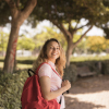 Jovem estudante loira sorrindo, com mochila vermelha, no campus